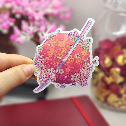 Sticker of a pink sticker with flowers and a katana sword held by a hand, with a blurred background.